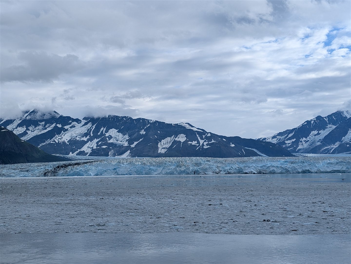 A tidewater glacier and snow-capped mountains along the Alaskan coast