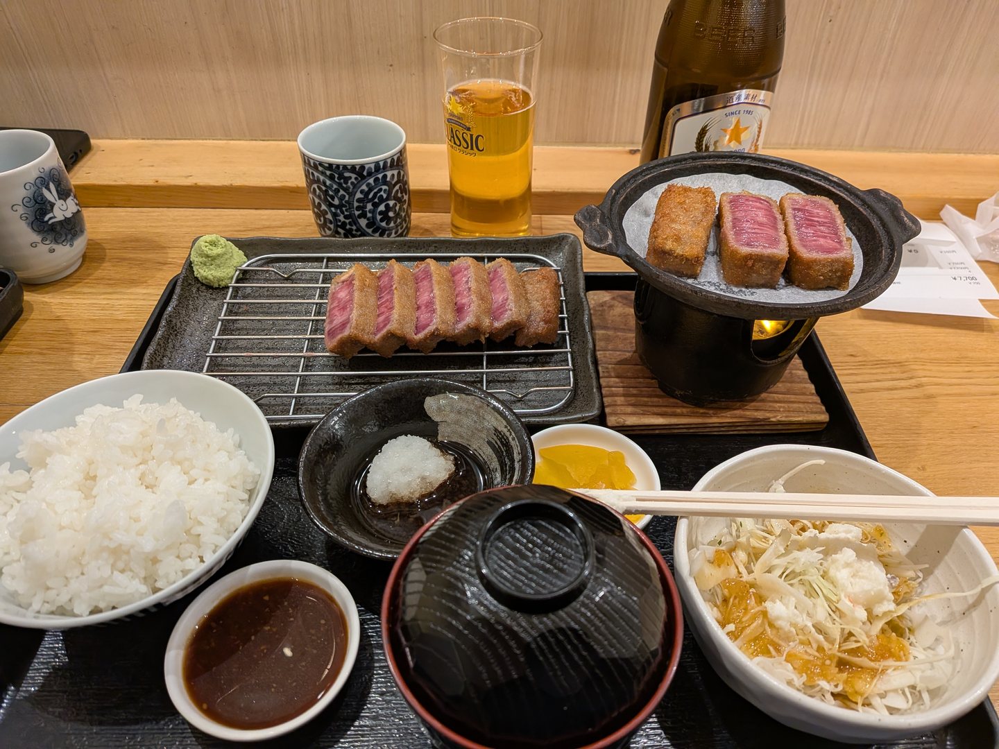 A gyukatsu set meal with sliced beef cutlet, rice, miso soup, sides and a beer
