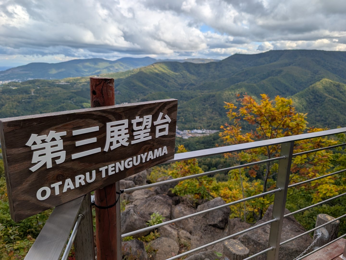 The Otaru Tenguyama observation deck sign, with autumn color and mountains behind