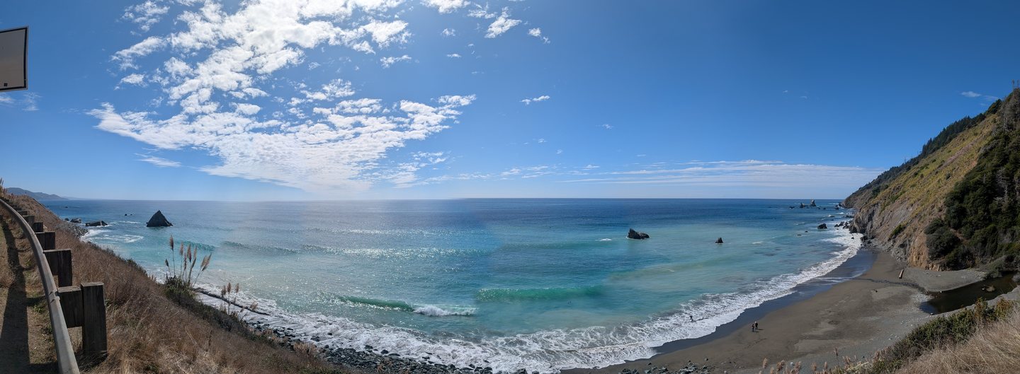 A wide panorama of a blue-green bay and beach below a coastal bluff