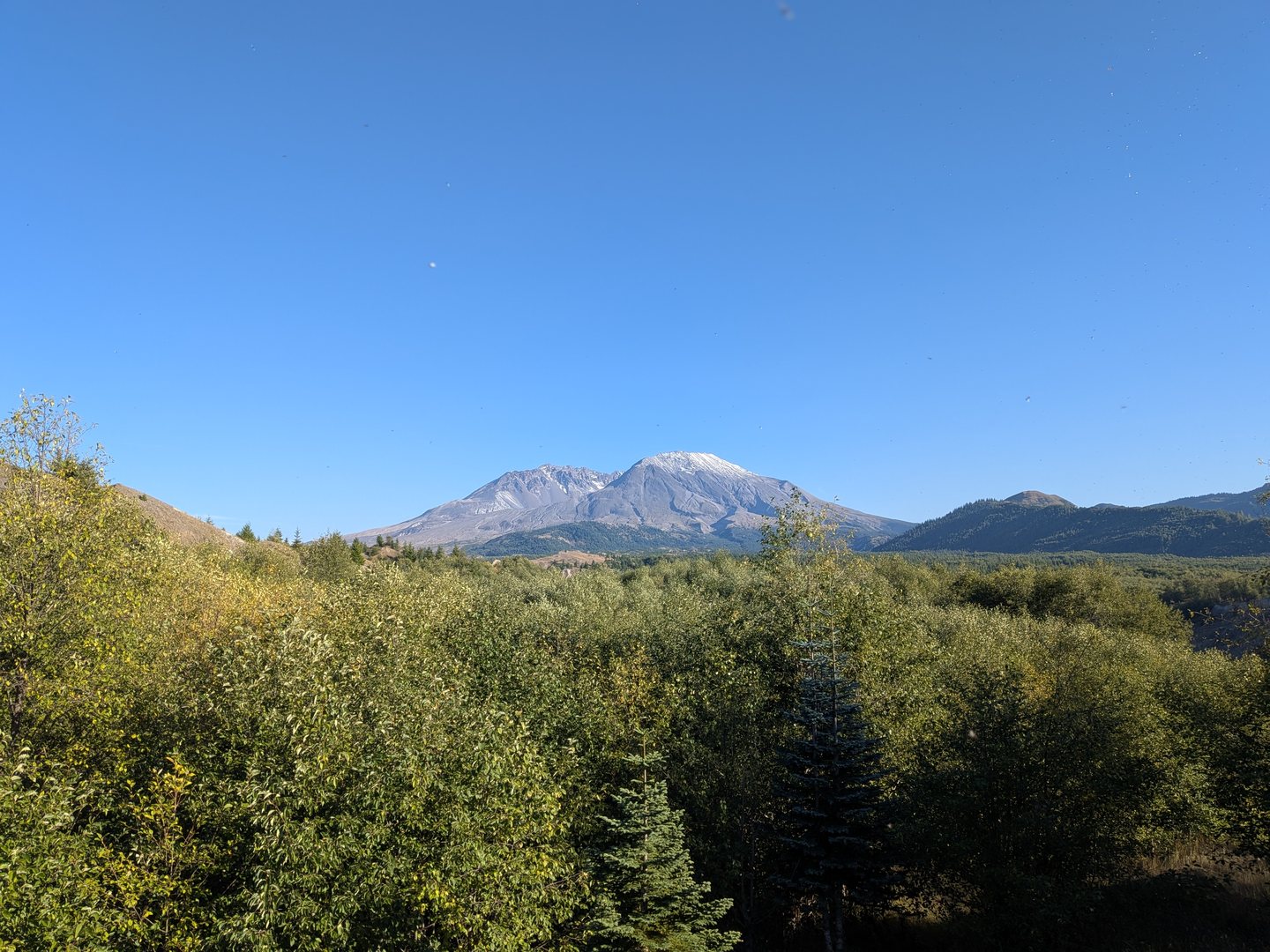 Mount St. Helens rising above hills and trees under a clear blue sky