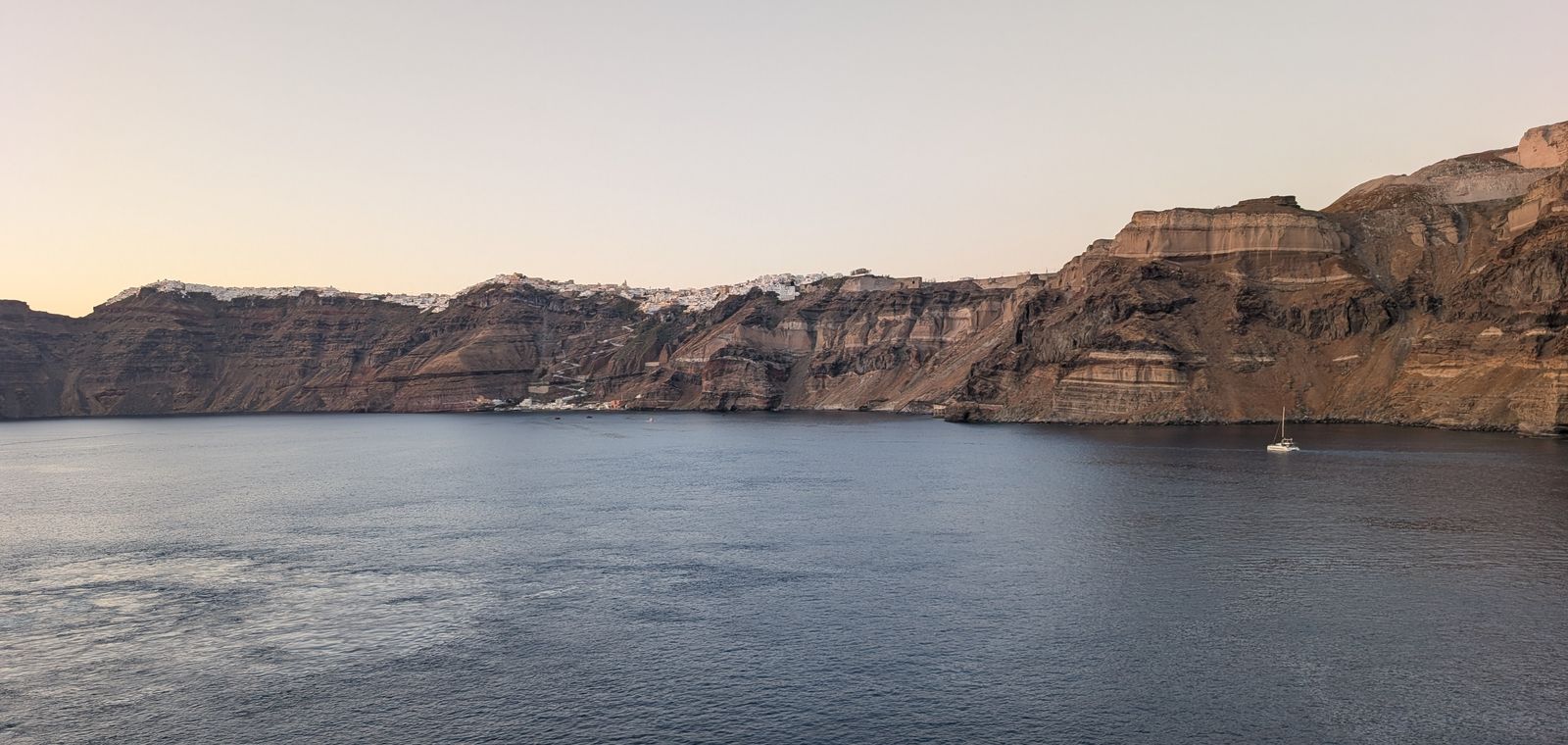 Calm water below the layered volcanic cliffs of the Santorini caldera at dusk